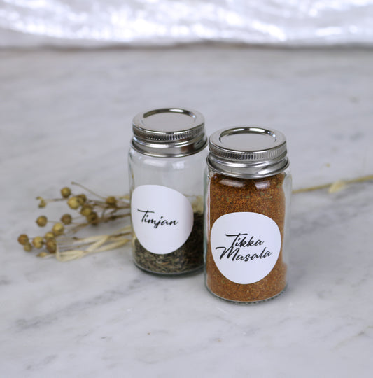 Två små kryddburkar med runda vita etiketter med timjan och tikka masala.